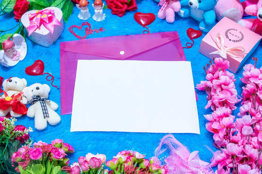 Blank white A4 paper on the top of a pink envelope surrounded by valentine themed decorations