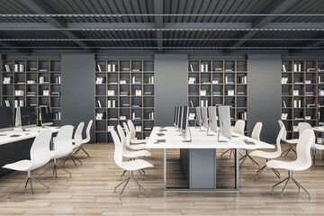 Side view on modern spacious coworking office with modern computers on white work tables, light chairs on wooden floor and huge book case on dark wall background. 3D rendering
