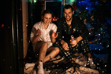 Merry Christmas and happy new year. Young couple in love celebrating Christmas or new year eve at home. Romantic couple in pajamas having fun with confetti at home.