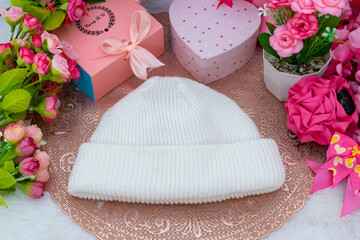 White blank beanie above a small round tablecloth hat surrounded by gift boxes and flowers