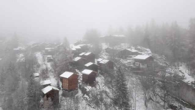 Snowy landscape with snowy chalets in the Swiss Alps. A mountain village with stables and chalets in fog and snow