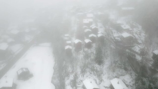 Small Swiss village in the mountains with fog and snow. Small chalets, cottages and alpine cabins. Aerial Shot