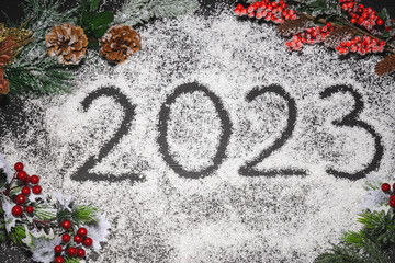 New year 2023 text written in snow with decoration of christmas tree, fir cones and wild berries with snowflakes