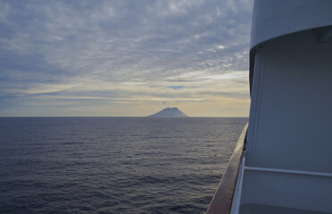 Stromboli volcano at horizon with clouds of smoke coming from summit seen from outdoor deck of...