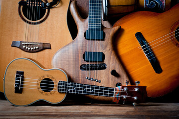 Fototapeta na wymiar Acoustic and electric guitars, ukulele and djembe standing side by side on a wooden background.