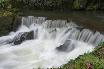 Beautiful waterfall in long exposure mode with leaves falling on the ground in different colors. Located in Cantabria, Spain