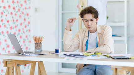 Obraz premium Millennial Asian young thoughtful stressed worried professional male dressmaker designer seamstress with measuring tape sitting thinking creating idea solving problem in tailor studio workshop office