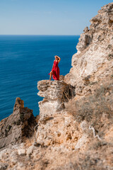 Fototapeta premium A woman in a red flying dress fluttering in the wind, against the backdrop of the sea.