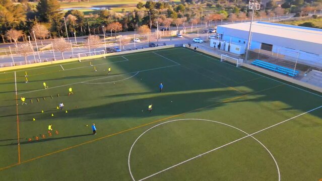 Rotating drone shot of children playing football on a field during golden hour in Santa Ponsa, Mallorca, Spain.