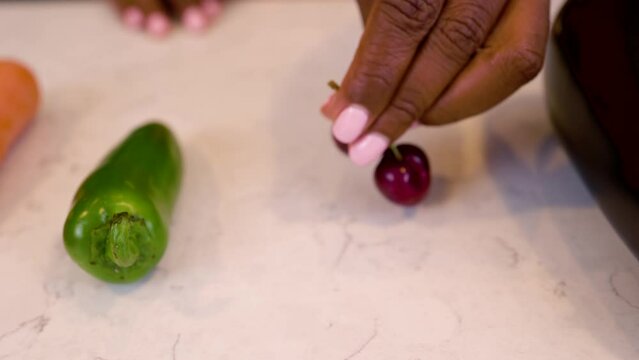 black woman hand is seductively grabbing cherry vegetables on a marble kitchen table. she slowly picks up the food and places back down on the surface