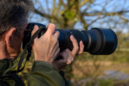 Man with telephoto lens captures a picture at the estuary. Middle aged gentleman   is bird watching and pans his camera as the bird fly's by. All Natural wildlife colours.