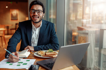 Smiling businessman working with graphs and charts at modern cafe. Blurred background