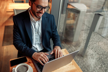 Smiling Indian businessman working on laptop in coffee shop working space