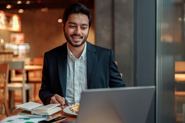 Fototapeta premium Handsome indian businessman working on laptop in cozy cafe sitting near window