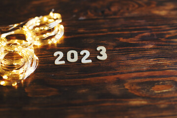 wooden number 2023 on christmas shiny wooden background. with sparkle festive gold garland