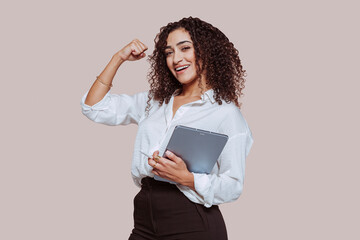 Portrait of a young cheerful arabic businesswoman, showing strong bicep muscle, works using digital...