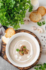 Mushroom cream soup with cream, croutons and herbs on a white wooden background. Delicious comfort food.