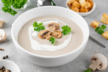 Mushroom cream soup with cream, croutons and herbs on a white wooden background. Delicious comfort food.