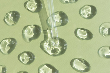 Drops of serum or hyaluronic acid gel with a pipette on a green background. Smears of cosmetic skin care products. Wellness and beauty concept