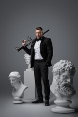Obraz premium Shot of professional killer man holding rifle on his shoulder and greek busts.