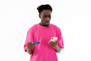 Serious african man holding credit card and cellphone in hands carefully writing card number posing on white background in studio isolated for bank advertisiment.