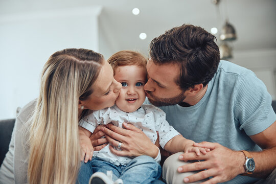 Mom, dad and baby kiss on sofa in living room of happy family home, young parents and child together. Love, happiness and couple kissing kid with smile while sitting on couch in New York apartment.