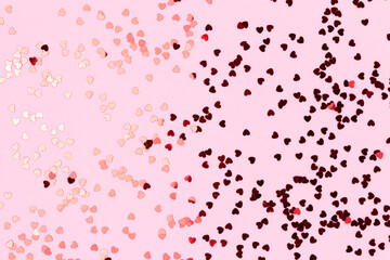 Metallic red confetti in a heart shaped scattered on a pink background. Festive texture.