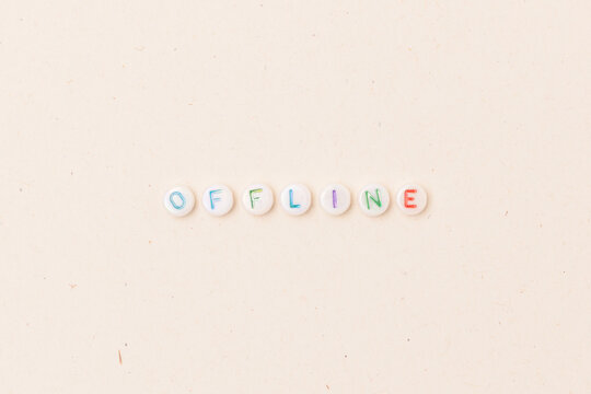 Word Offline. Quote made of white round beads with multicolored letters on a beige background. Digital detox concept.
