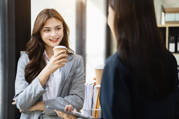 Female colleague during work break standing holding coffee mugs in work area smiling various business team talking joyfully enjoying conversation friendly relations in the office.