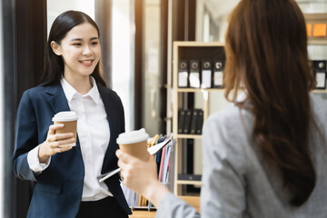 Female colleague during work break standing holding coffee mugs in work area smiling various business team talking joyfully enjoying conversation friendly relations in the office.