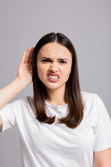 Photo of curious angry young woman keeps hand near ear bends forward eavesdropes tries to overhear...