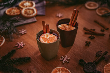 Christmas mulled wine in old cups with cinnamon straws stands on an old table, surrounded by spruce twigs, Christmas decor and dried oranges. Christmas cozy atmosphere. Christmas hot alcoholic drink