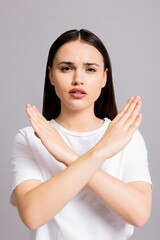 Portrait of young serious young woman shows stop gesture. making cross with arms and looking displeased at camera, prohibiting forbides something, standing over grey background.