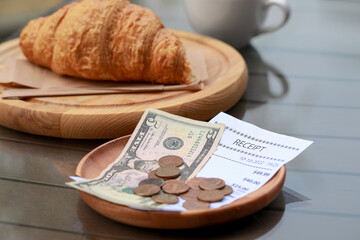 Tips, receipt and croissant on wooden table, closeup