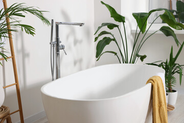 Stylish ceramic tub and beautiful houseplants in bathroom. Interior design