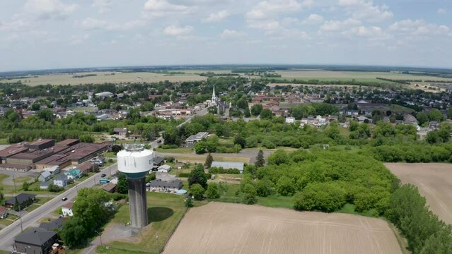 Aerial View Of Water Tower Beside Farm Fields Near Fast Growing Town Of Ebrun, Ontario. Rural Community With Mix If Agriculture And Business.