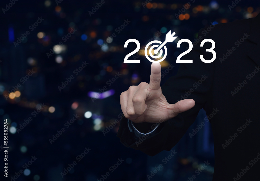 Wall mural businessman pressing 2023 letter with goal icon over blur colorful night light modern city tower and