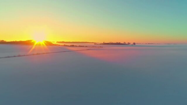 Glowing golden sunset on the horizon of an empty snowy landscape of rural farmland fields - aerial view
