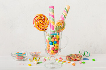 Colorful candies in cup on table on light background background. Large swirled lollipops. Creative concept of a jar full of delicious sweets from the candy store