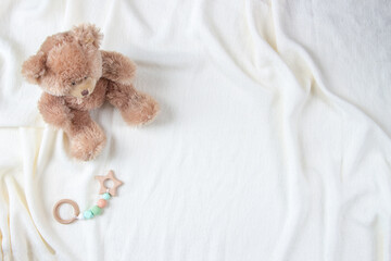Teddy bear and natural wooden rattle toy on white blanket throw background. Top view