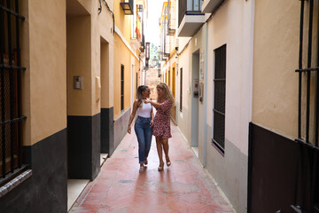 Two beautiful women strolling through the narrow streets of Seville. The women are on vacation in Europe and visit the historical center of the city.