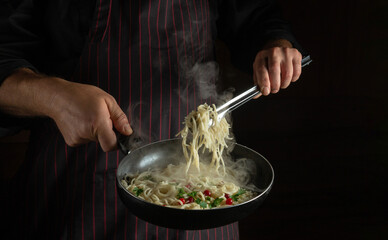 The cook prepares spaghetti with spices and seasonings in a frying pan. Recipe or menu for a restaurant or cafe on a dark background. Copy space