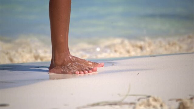 Slow motion close up of a thin latin woman's feet playing with the sand with her toes while at the beach while baby sitting her son in Cancun