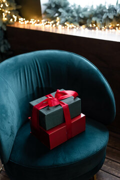 Two Gift Boxes Wrapped With Red Ribbon On A Chair By A Window With A Light Garland