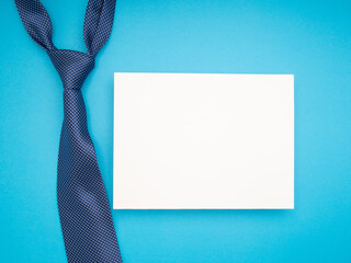 Top view of a necktie and a blank white paper over a blue background