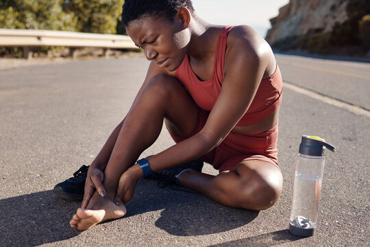 Black woman, runner and foot injury outdoor, pain and training on road, marathon and water bottle. African American female, girl and athlete with discomfort on heel, suffering and agony for fitness.
