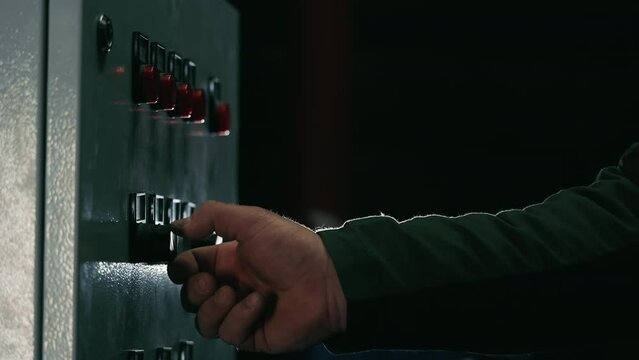 Industrial start or stop button in a dark room. Turning the device on or off with a male hand.
