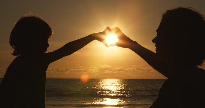 mother and little son silhouette at sunset, Hands of woman and her child made a heart shape at sunset. Happiness and freedom, dream of motherhood concept, happy mother and child, emotional scene