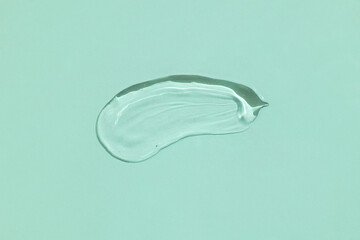 A drop of clear cosmetic aloe vera gel on a green background. Flat lay, space for text.