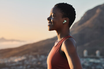 Fototapeta Headphones, fitness or zen black woman on a mountain for peaceful, calm and breathing in relaxing fresh air. Breathe, healthy or happy sports athlete with smile streaming radio music, song or podcast obraz
